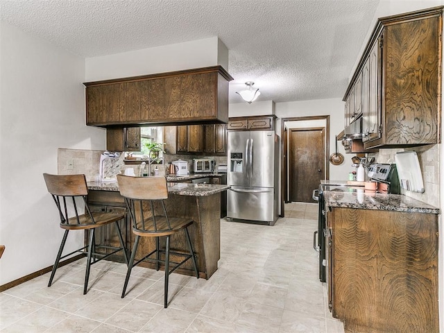 kitchen with dark brown cabinetry, a breakfast bar area, appliances with stainless steel finishes, a peninsula, and dark stone counters