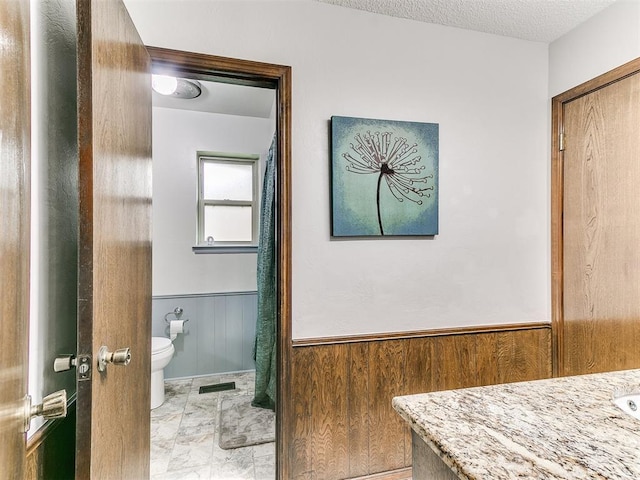bathroom featuring visible vents, wood walls, marble finish floor, wainscoting, and toilet