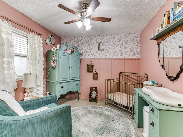 bedroom featuring a textured ceiling, wainscoting, light carpet, and wallpapered walls