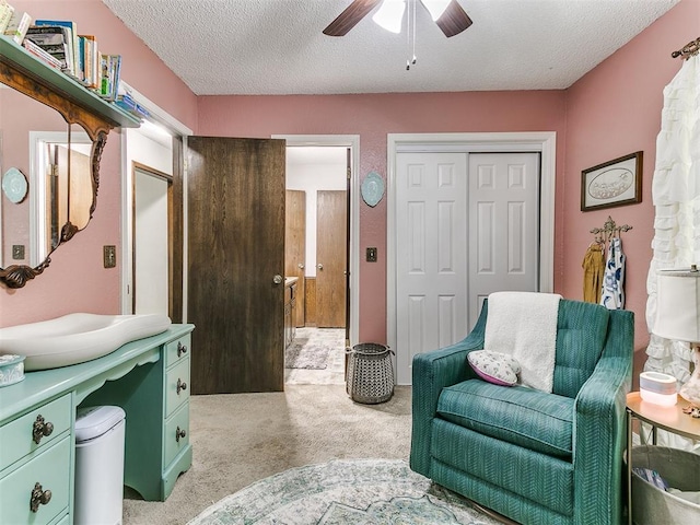 living area featuring ceiling fan, light carpet, and a textured ceiling