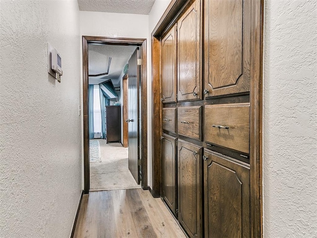 hall with light wood-type flooring, a textured ceiling, and a textured wall