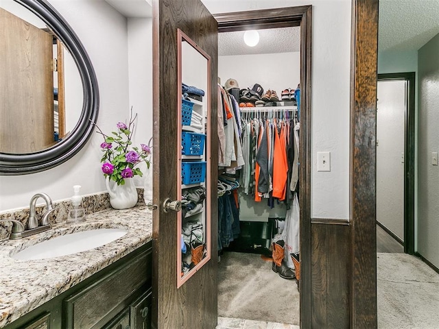 bathroom with vanity, a textured ceiling, and a walk in closet