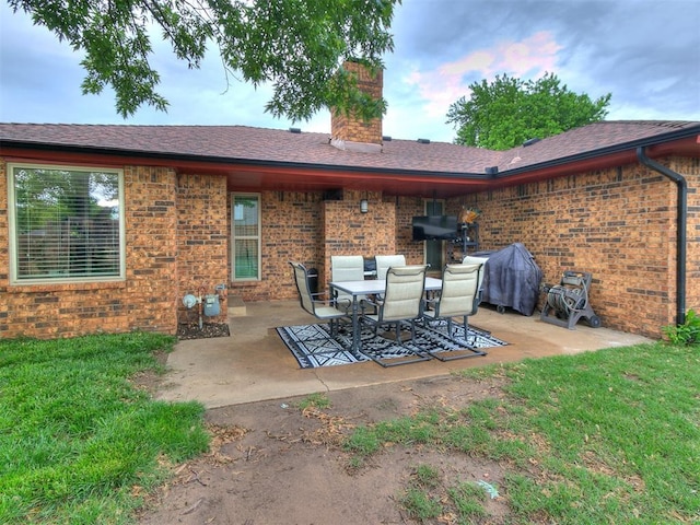 back of property featuring a lawn, brick siding, a chimney, and a patio area