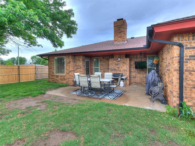 rear view of house with fence, a chimney, brick siding, a patio area, and a lawn