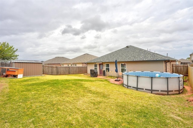 back of property with a fenced backyard, a yard, a fenced in pool, a shingled roof, and an outbuilding
