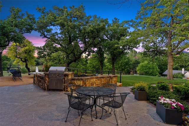 2203 E Wilshire Blvd, Oklahoma City, OK 73111 - patio terrace at dusk featuring area for grilling, exterior kitchen, outdoor dining area, a lawn, and view of wooded area