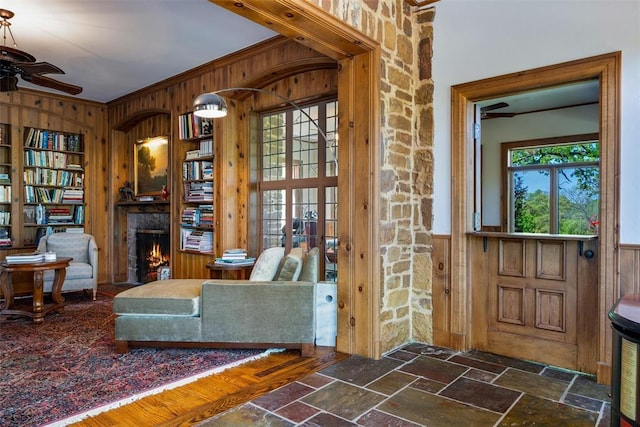 2203 E Wilshire Blvd, Oklahoma City, OK 73111 - living area with wooden walls, a ceiling fan, stone tile flooring, a stone fireplace, and ornamental molding