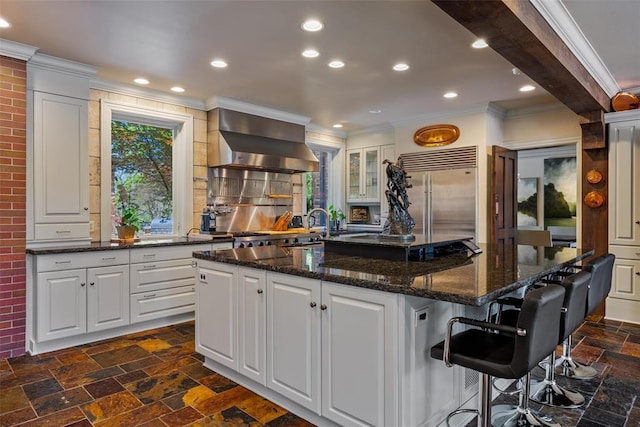 2203 E Wilshire Blvd, Oklahoma City, OK 73111 - kitchen featuring wall chimney exhaust hood, built in fridge, stone tile flooring, crown molding, and a center island