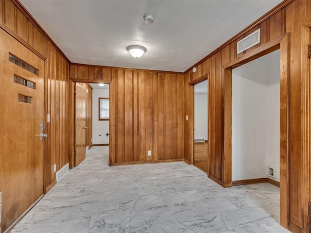unfurnished room with visible vents, wood walls, marble finish floor, crown molding, and baseboards