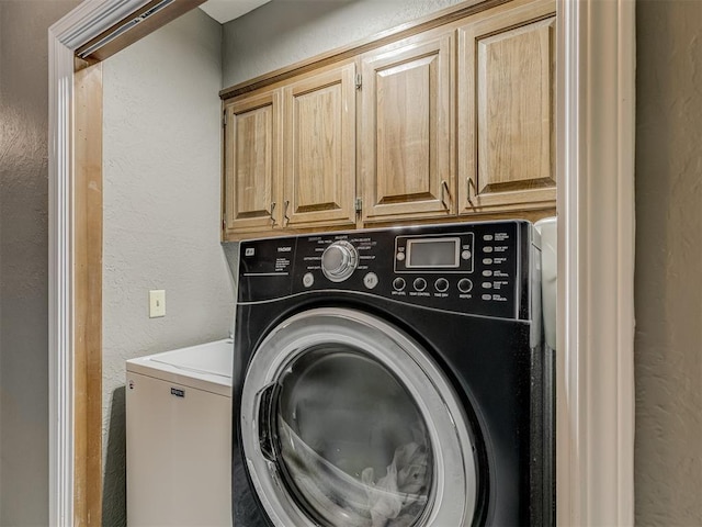 clothes washing area with a textured wall, cabinet space, and washer and clothes dryer