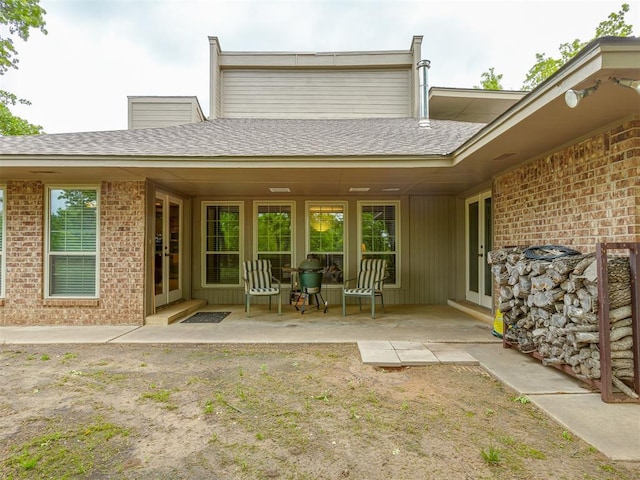 back of property with brick siding, roof with shingles, and french doors
