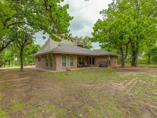 rear view of house with brick siding, a shingled roof, and a patio area