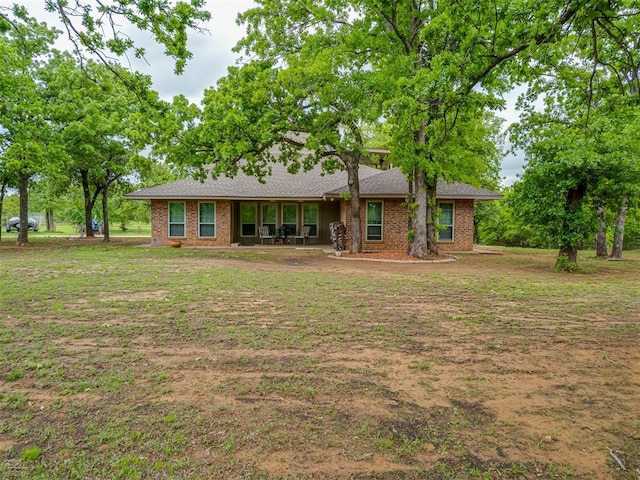 back of house featuring a lawn, roof with shingles, brick siding, and a patio
