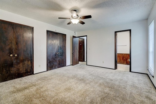 unfurnished bedroom featuring light colored carpet, a textured ceiling, ceiling fan, and two closets