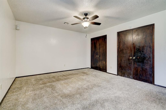 unfurnished bedroom featuring two closets, baseboards, a textured ceiling, a ceiling fan, and carpet