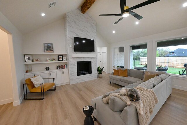 living room featuring visible vents, beamed ceiling, ceiling fan, light wood-style flooring, and a premium fireplace