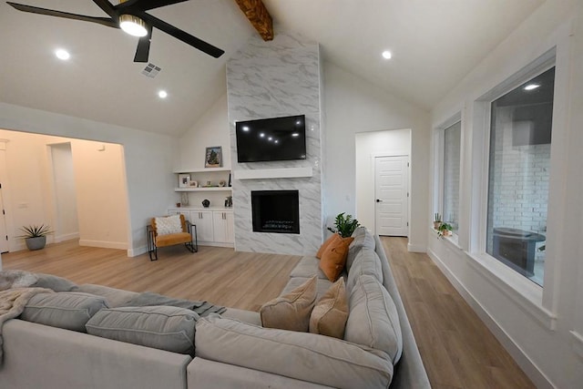 living area featuring beam ceiling, baseboards, a high end fireplace, a ceiling fan, and light wood-style flooring
