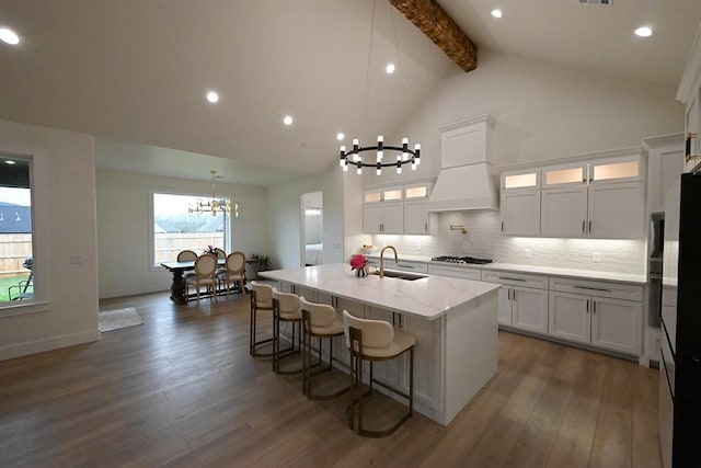 kitchen featuring an inviting chandelier, beam ceiling, a sink, dark wood finished floors, and a center island with sink