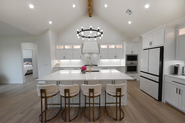 kitchen featuring appliances with stainless steel finishes, white cabinetry, beamed ceiling, visible vents, and a center island with sink