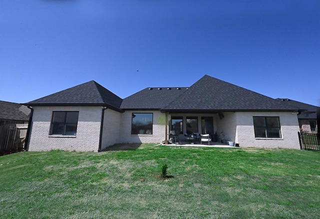 back of house with fence, a lawn, roof with shingles, and brick siding