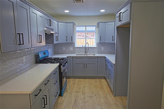 kitchen featuring stainless steel gas stove, under cabinet range hood, a sink, light wood finished floors, and gray cabinetry