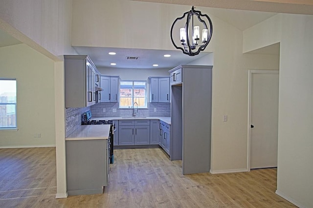 kitchen with backsplash, gas range, a sink, light countertops, and a chandelier