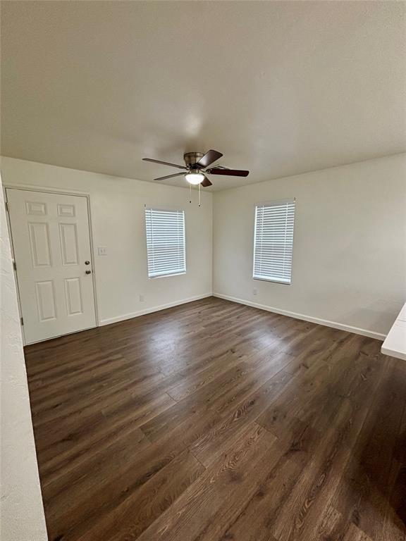 spare room featuring a ceiling fan, baseboards, and dark wood-type flooring