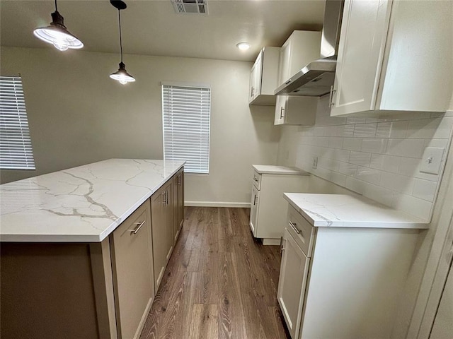 kitchen with a kitchen island, backsplash, light stone countertops, dark wood finished floors, and white cabinetry