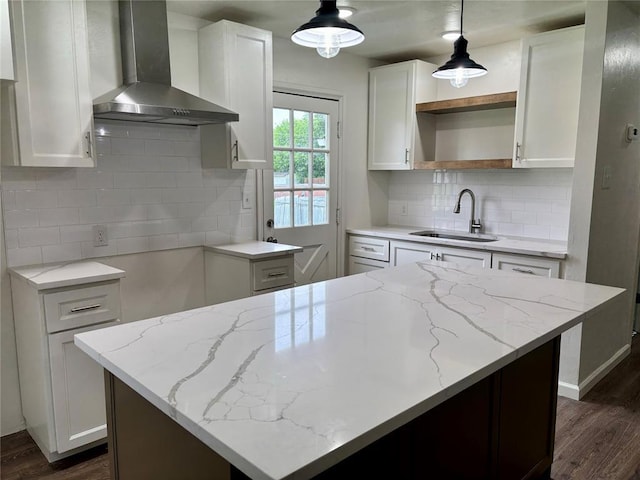 kitchen with a sink, light stone counters, wall chimney range hood, and dark wood-type flooring