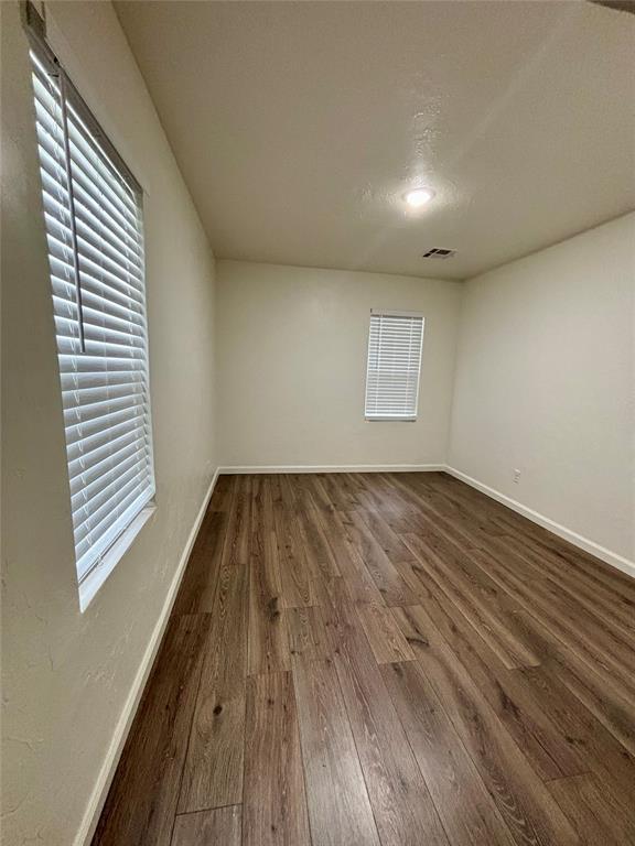 spare room with baseboards, dark wood-style flooring, and visible vents