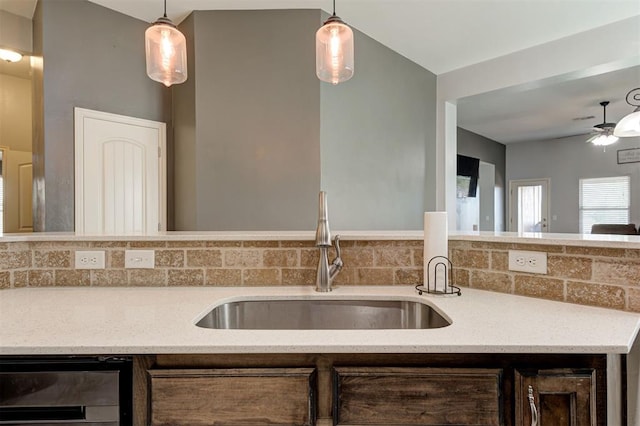 kitchen featuring wine cooler, dark brown cabinets, light stone countertops, a sink, and backsplash