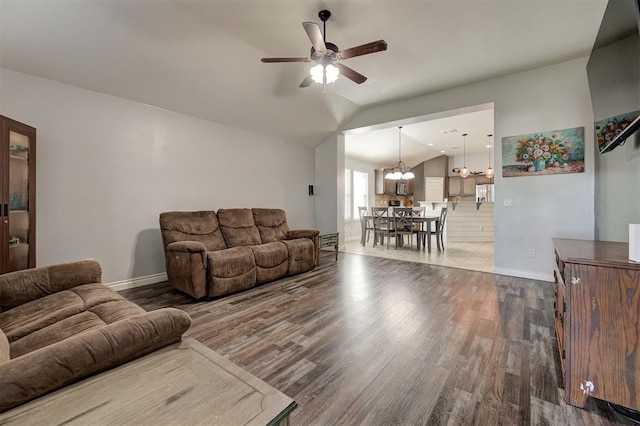 living area with baseboards, vaulted ceiling, wood finished floors, and ceiling fan with notable chandelier