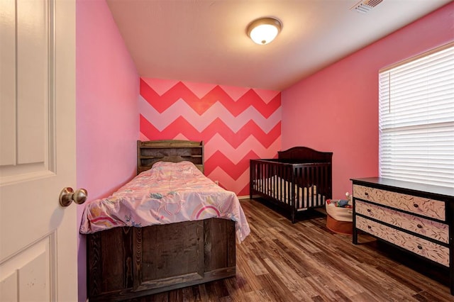 bedroom with an accent wall, wood finished floors, and visible vents