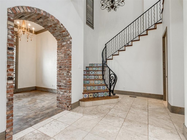 staircase with an inviting chandelier, arched walkways, baseboards, and a towering ceiling