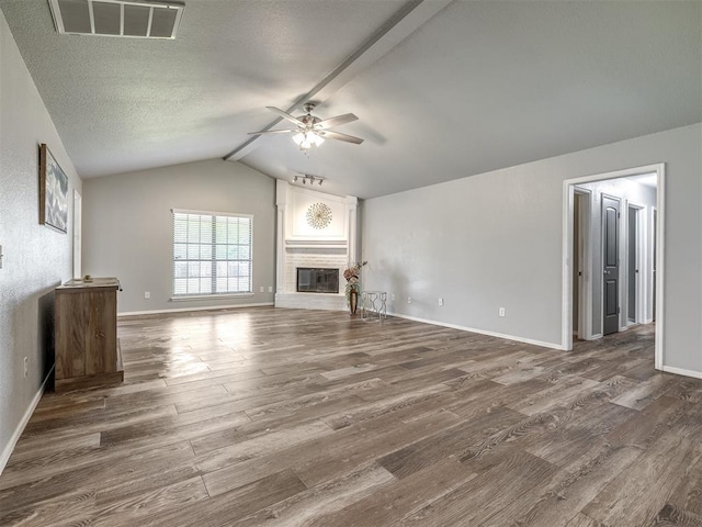unfurnished living room featuring a glass covered fireplace, a ceiling fan, vaulted ceiling with beams, wood finished floors, and visible vents