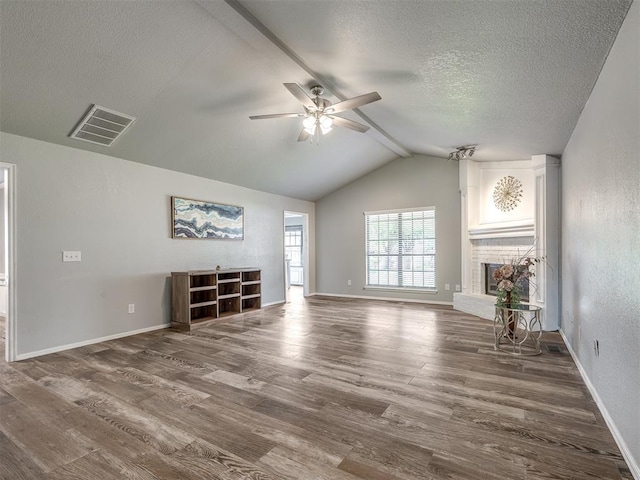 unfurnished living room with wood finished floors, a fireplace, ceiling fan, vaulted ceiling with beams, and a textured ceiling