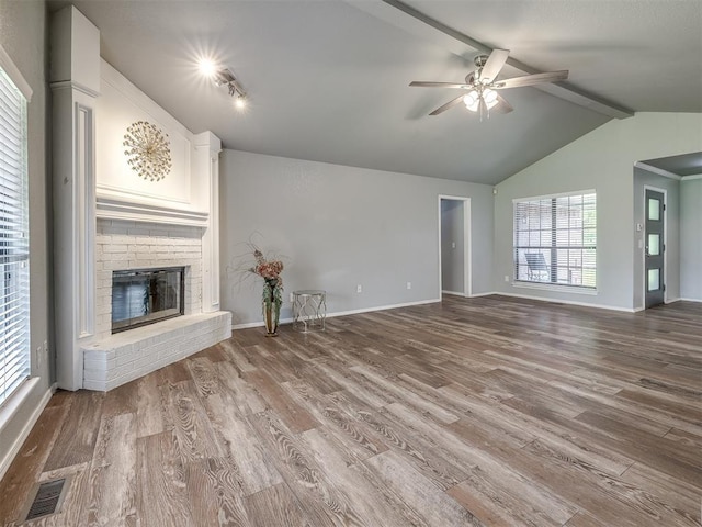 unfurnished living room featuring visible vents, a brick fireplace, wood finished floors, lofted ceiling with beams, and a ceiling fan