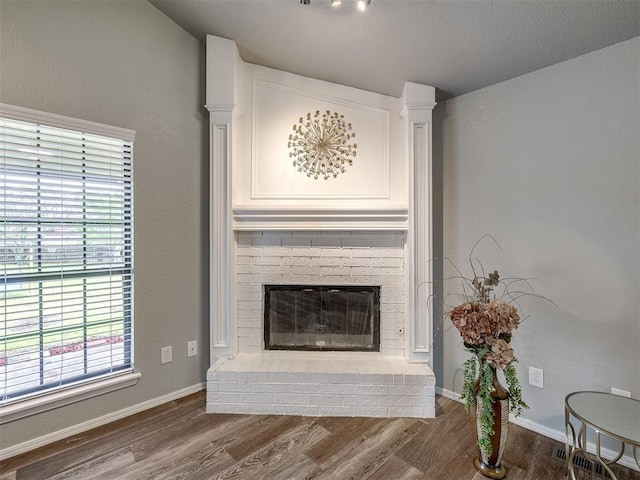 living area with a brick fireplace, baseboards, a healthy amount of sunlight, and wood finished floors