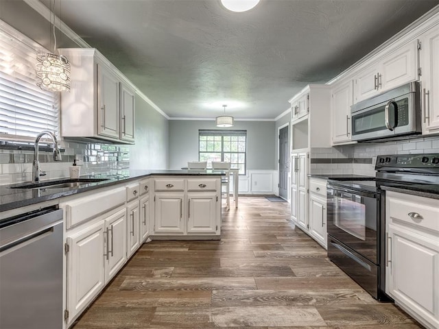 kitchen with appliances with stainless steel finishes, dark countertops, a sink, a peninsula, and white cabinetry