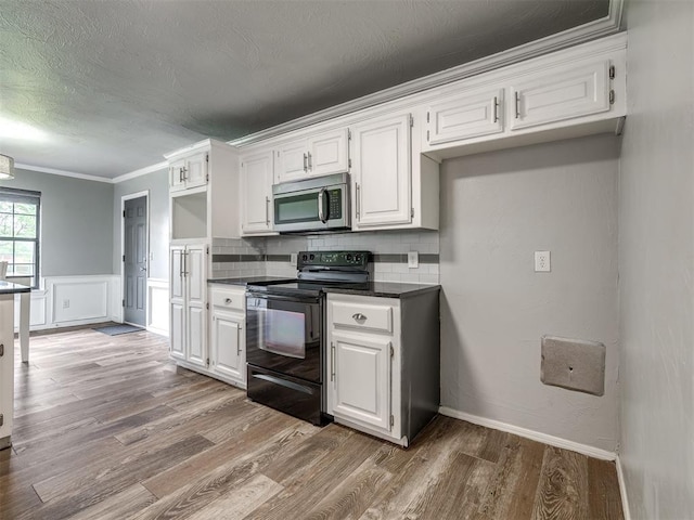 kitchen featuring white cabinets, stainless steel microwave, dark countertops, and black range with electric stovetop