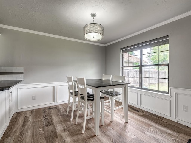 dining room featuring a wainscoted wall, ornamental molding, a decorative wall, and dark wood-type flooring