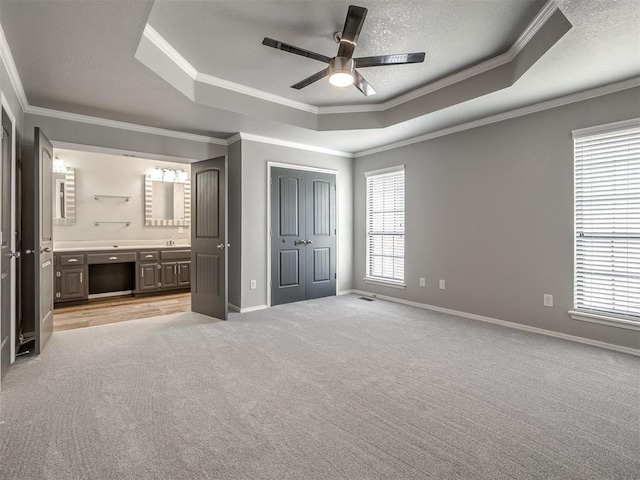 unfurnished bedroom with ornamental molding, a raised ceiling, light carpet, and multiple windows