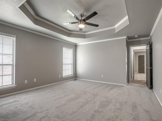 unfurnished bedroom with a textured ceiling, crown molding, a raised ceiling, baseboards, and light carpet