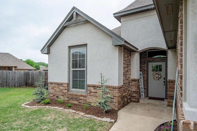 entrance to property featuring a lawn, brick siding, fence, and stucco siding