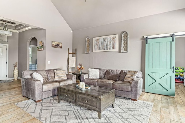 living area featuring wood finished floors, baseboards, high vaulted ceiling, a barn door, and arched walkways