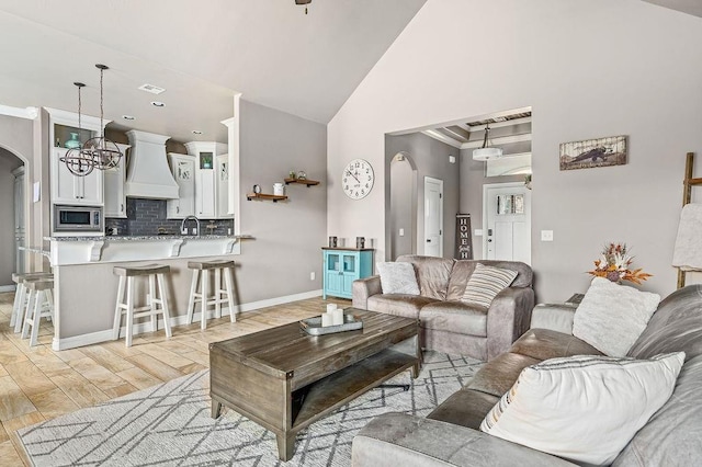 living area with arched walkways, high vaulted ceiling, baseboards, light wood-type flooring, and visible vents