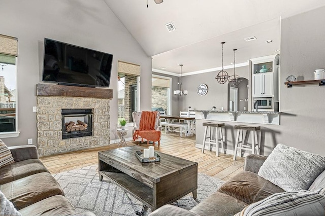 living room featuring visible vents, light wood-style flooring, lofted ceiling, and a stone fireplace