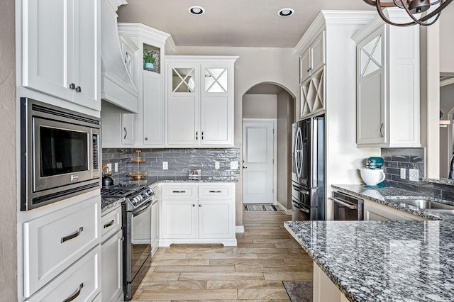 kitchen featuring a sink, arched walkways, dark stone countertops, stainless steel appliances, and backsplash