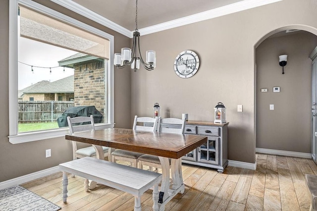 dining area featuring a notable chandelier, arched walkways, baseboards, light wood-type flooring, and ornamental molding