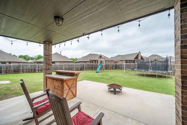 view of patio / terrace with a playground, a trampoline, a fenced backyard, and an outdoor fire pit